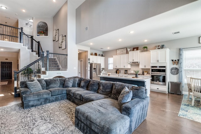 living room featuring dark wood-style flooring, recessed lighting, visible vents, a high ceiling, and stairs