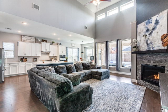 living room with sink, a fireplace, a towering ceiling, ceiling fan, and dark hardwood / wood-style floors