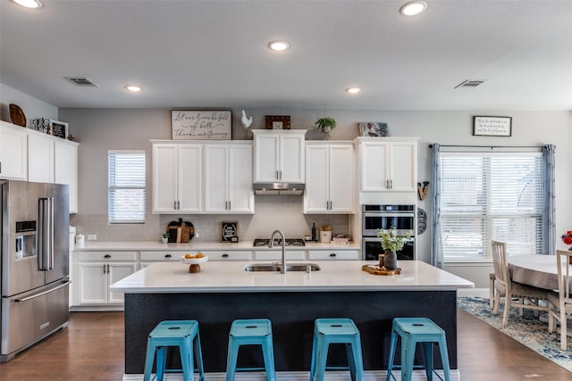 kitchen featuring a breakfast bar, a kitchen island with sink, white cabinets, appliances with stainless steel finishes, and sink