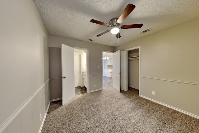 unfurnished bedroom with a textured ceiling, connected bathroom, ceiling fan, dark carpet, and a closet