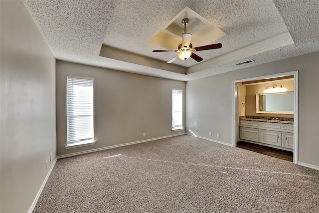 unfurnished bedroom with ceiling fan, multiple windows, a raised ceiling, and carpet