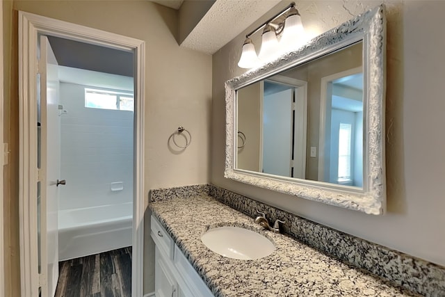 bathroom with vanity, a textured ceiling, hardwood / wood-style floors, and  shower combination