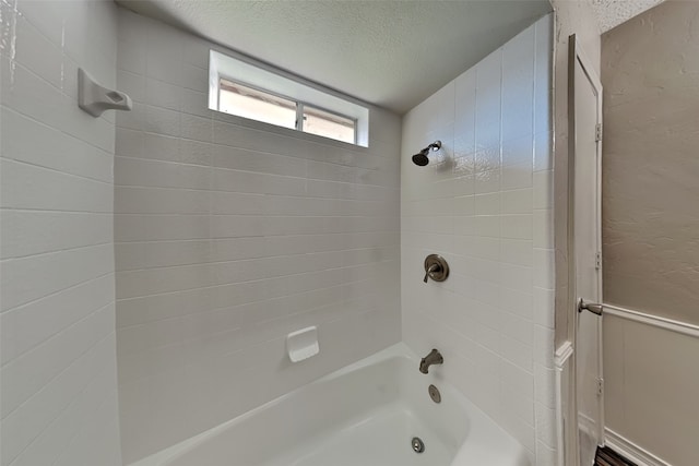 bathroom with a textured ceiling and tiled shower / bath