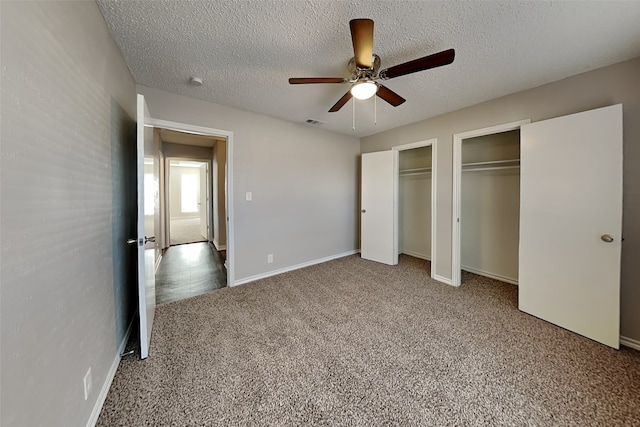 unfurnished bedroom featuring a textured ceiling, ceiling fan, carpet, and two closets