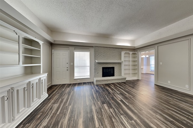 unfurnished living room with a textured ceiling, a brick fireplace, built in features, and dark hardwood / wood-style floors