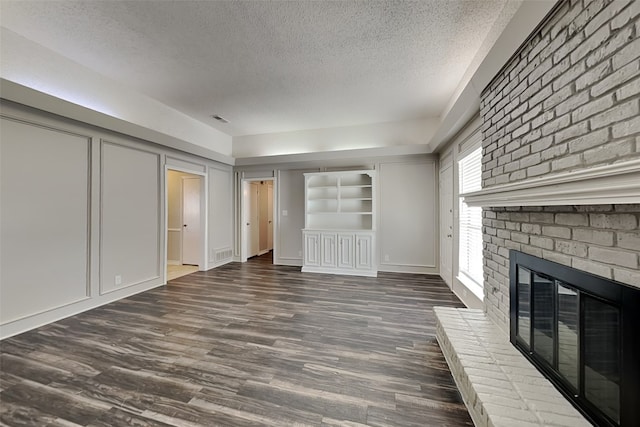 unfurnished living room with a textured ceiling, dark wood-type flooring, a brick fireplace, and built in features