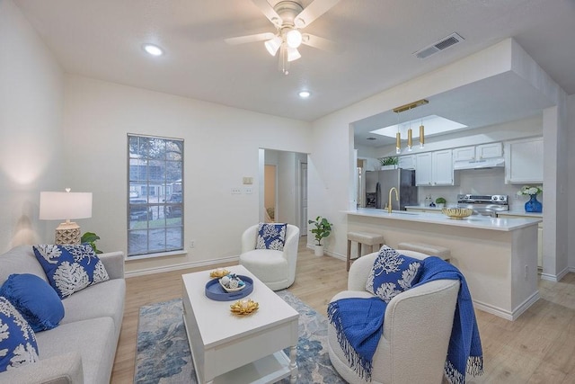 living room featuring light hardwood / wood-style floors, ceiling fan, and sink