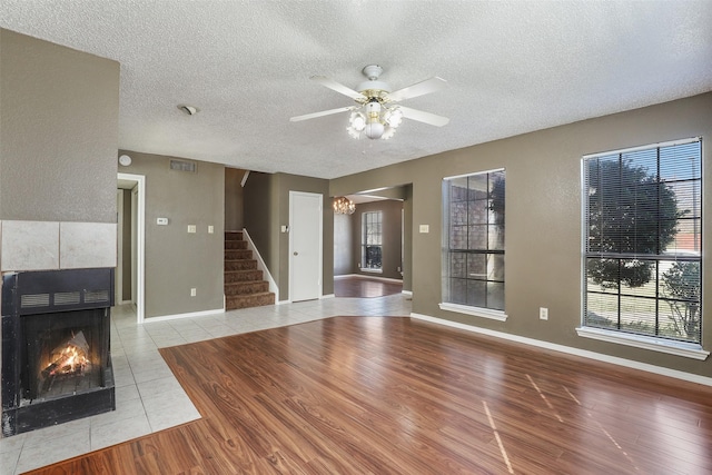 unfurnished living room featuring light hardwood / wood-style floors, ceiling fan, a textured ceiling, and a tiled fireplace