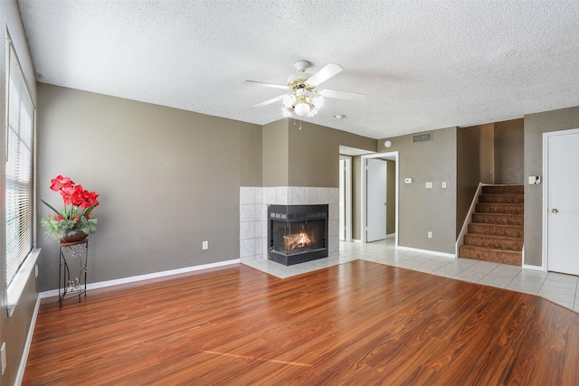 unfurnished living room with ceiling fan, light wood-type flooring, a fireplace, and a textured ceiling