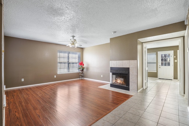 unfurnished living room with ceiling fan, a textured ceiling, light wood-type flooring, and a fireplace