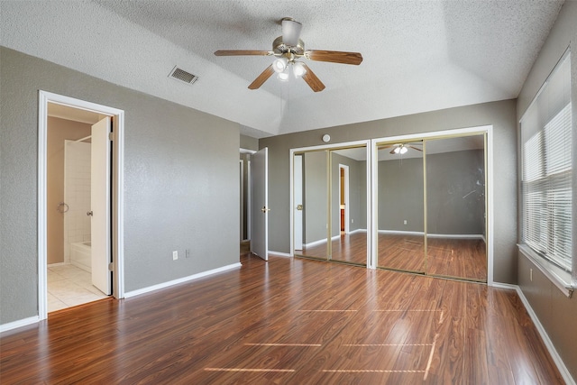 unfurnished bedroom featuring hardwood / wood-style floors, a textured ceiling, ensuite bath, two closets, and ceiling fan