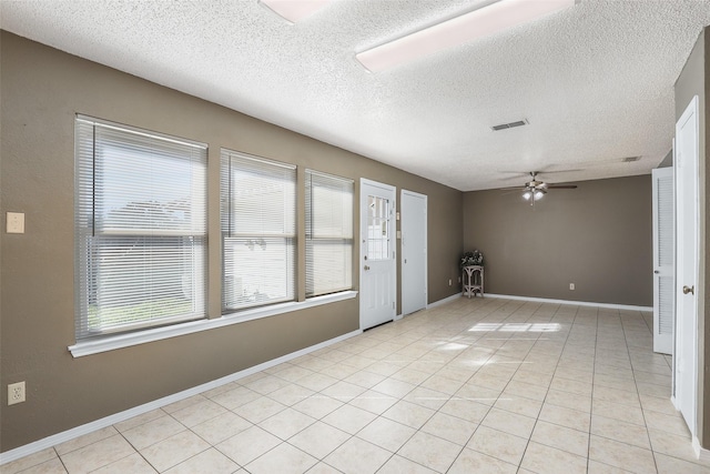 spare room featuring ceiling fan, light tile patterned floors, and a textured ceiling