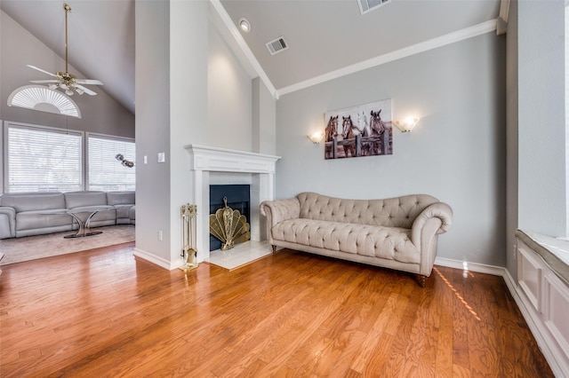 living room featuring lofted ceiling, wood-type flooring, ceiling fan, a tile fireplace, and crown molding