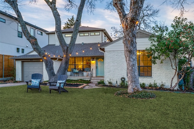 back house at dusk featuring a lawn and a garage