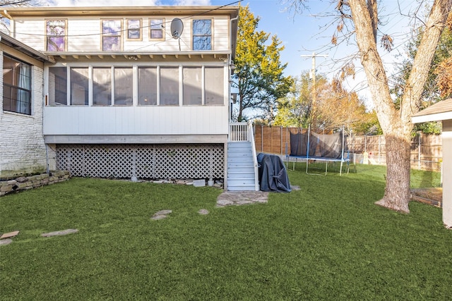 back of property featuring a lawn, a sunroom, and a trampoline