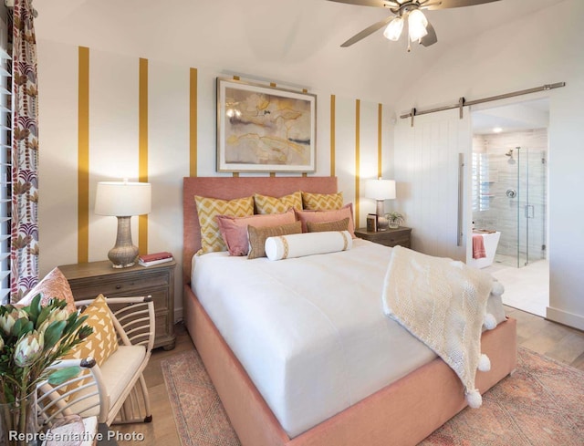 bedroom with lofted ceiling, connected bathroom, hardwood / wood-style flooring, ceiling fan, and a barn door