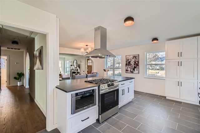 kitchen featuring island range hood, an inviting chandelier, dark tile patterned flooring, white cabinetry, and appliances with stainless steel finishes