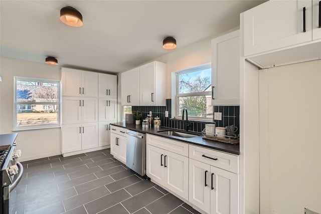 kitchen featuring dark tile patterned floors, backsplash, white cabinetry, appliances with stainless steel finishes, and sink