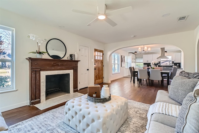 living room featuring a high end fireplace, ceiling fan with notable chandelier, and wood-type flooring