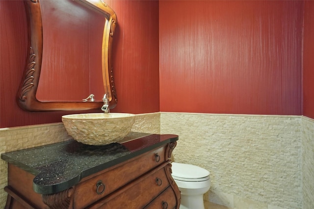 bathroom with vanity, toilet, and tile walls