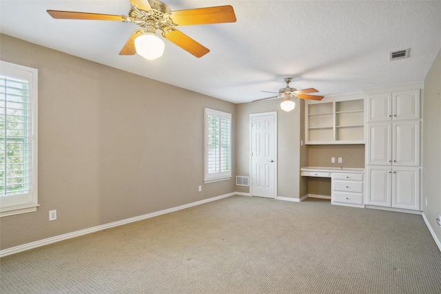 interior space with ceiling fan, built in desk, and light carpet