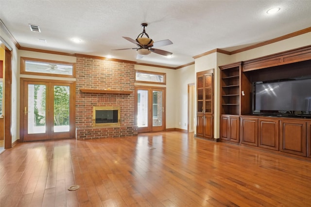 unfurnished living room with ceiling fan, a textured ceiling, a brick fireplace, french doors, and light wood-type flooring