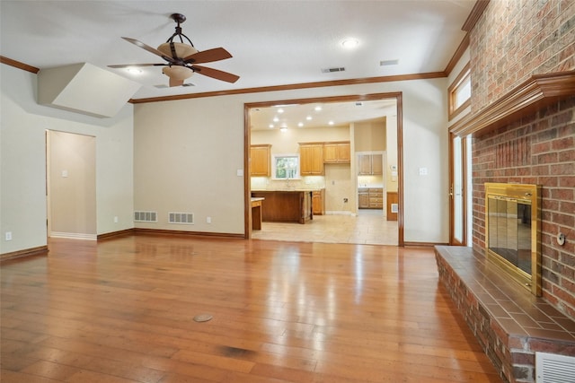 unfurnished living room with ceiling fan, ornamental molding, a brick fireplace, and light wood-type flooring