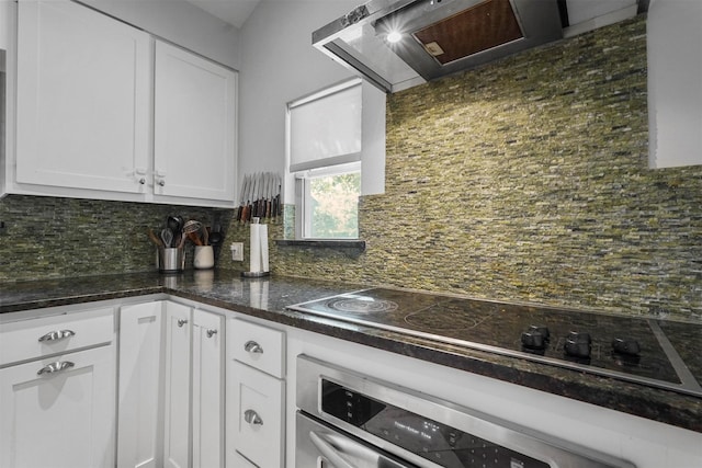 kitchen with wall chimney range hood, oven, decorative backsplash, black electric stovetop, and white cabinets