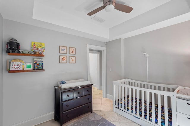 bedroom featuring a nursery area, a raised ceiling, light tile patterned flooring, and ceiling fan