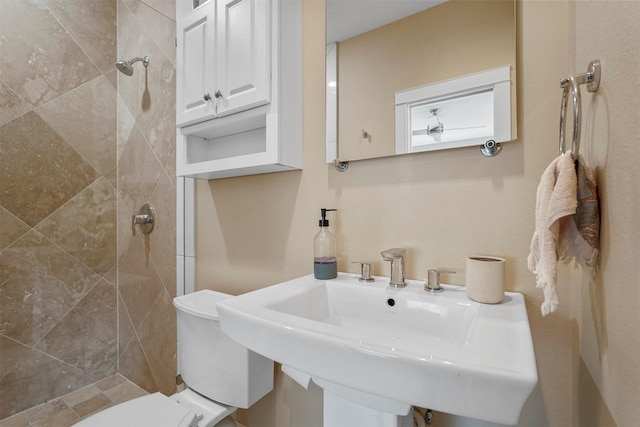 bathroom featuring sink, tiled shower, and toilet