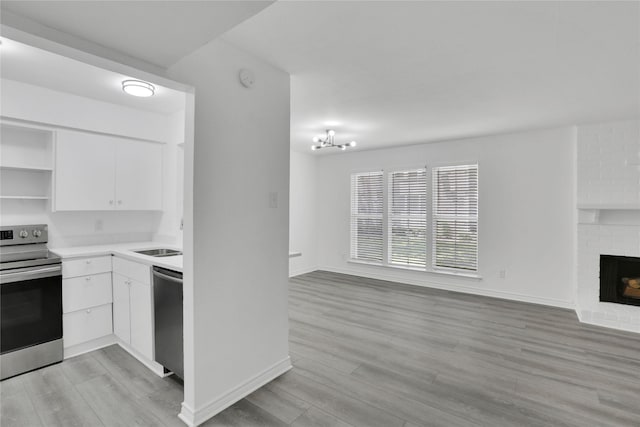 kitchen with white cabinets, light wood-type flooring, appliances with stainless steel finishes, and a fireplace