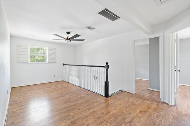 empty room with beam ceiling, ceiling fan, and wood-type flooring