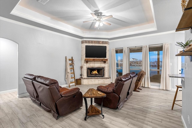 living room featuring a fireplace, ceiling fan, a tray ceiling, and ornamental molding