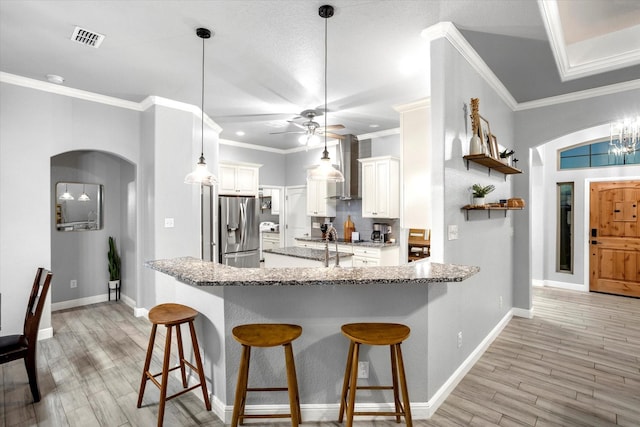 kitchen with decorative light fixtures, white cabinets, wall chimney exhaust hood, and stainless steel refrigerator with ice dispenser