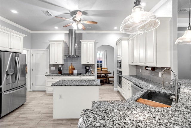 kitchen with appliances with stainless steel finishes, ornamental molding, white cabinets, wall chimney range hood, and sink