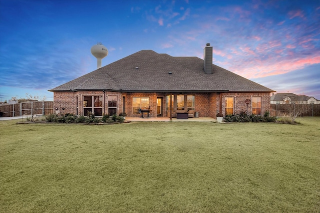 back house at dusk with a yard and a patio