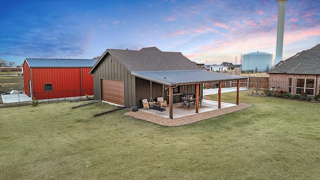 back house at dusk featuring an outdoor structure, a yard, a patio, and a garage