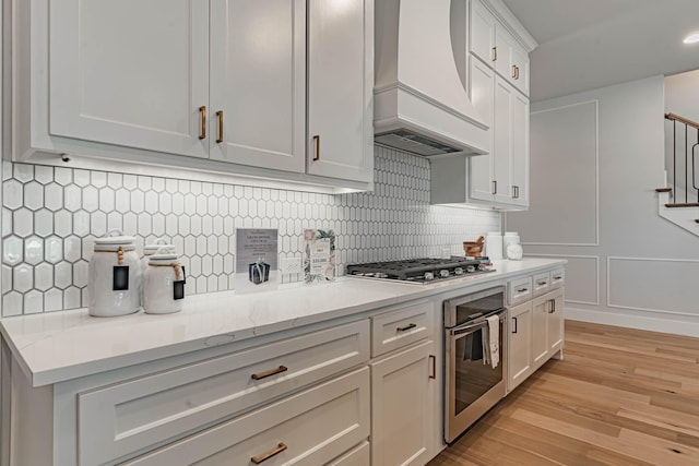 kitchen with appliances with stainless steel finishes, white cabinetry, backsplash, and premium range hood