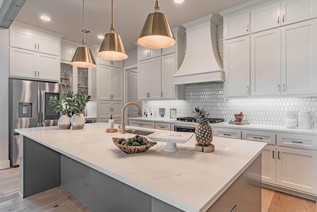 kitchen with sink, an island with sink, custom exhaust hood, and hanging light fixtures