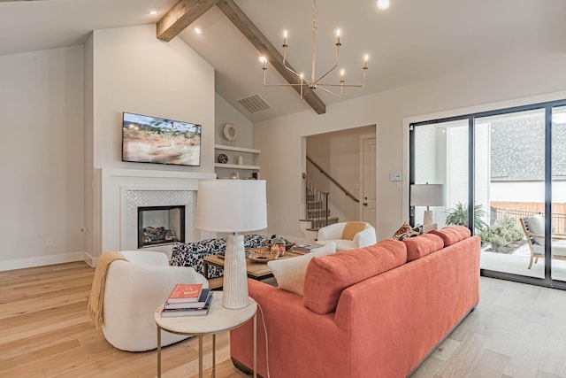 living room featuring a tile fireplace, an inviting chandelier, beamed ceiling, and light hardwood / wood-style flooring