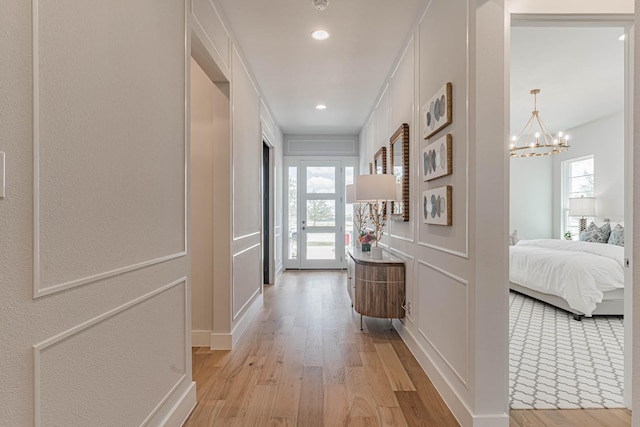 corridor with light hardwood / wood-style floors, an inviting chandelier, and a wealth of natural light