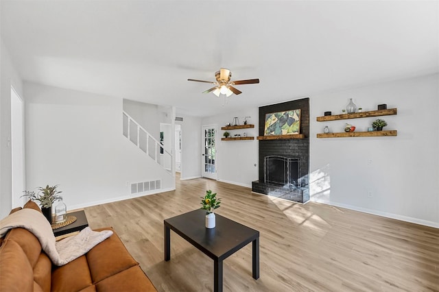 living room with ceiling fan, light hardwood / wood-style floors, and a brick fireplace