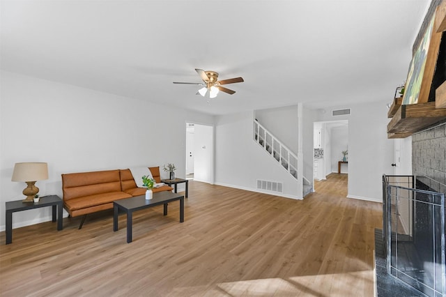 living room with ceiling fan, a brick fireplace, and light hardwood / wood-style floors