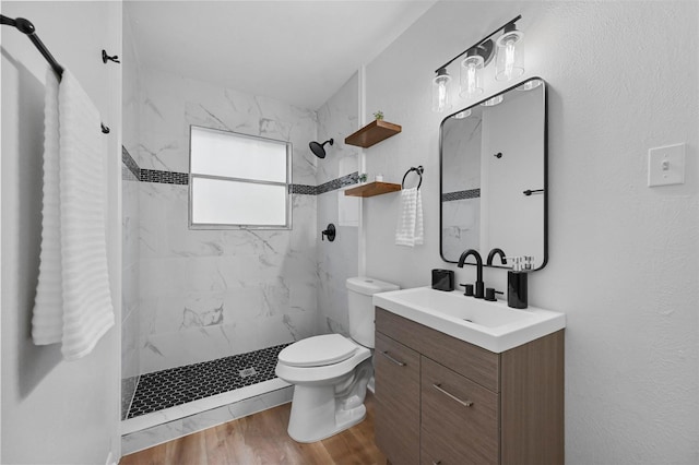 bathroom featuring a tile shower, toilet, vanity, and wood-type flooring