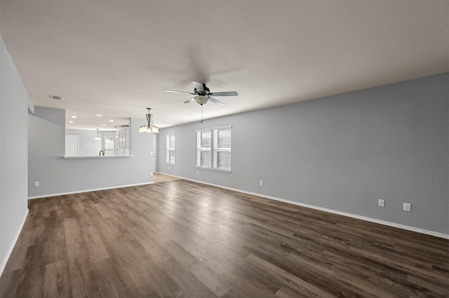 unfurnished living room with ceiling fan with notable chandelier and dark wood-type flooring