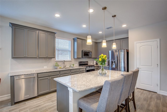 kitchen with light hardwood / wood-style floors, a center island, pendant lighting, stainless steel appliances, and light stone counters