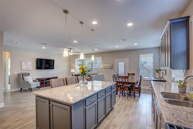 kitchen featuring ceiling fan, decorative light fixtures, a center island, sink, and light stone counters