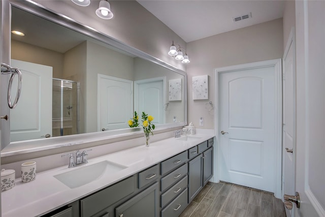 bathroom featuring double vanity, a stall shower, visible vents, wood tiled floor, and a sink