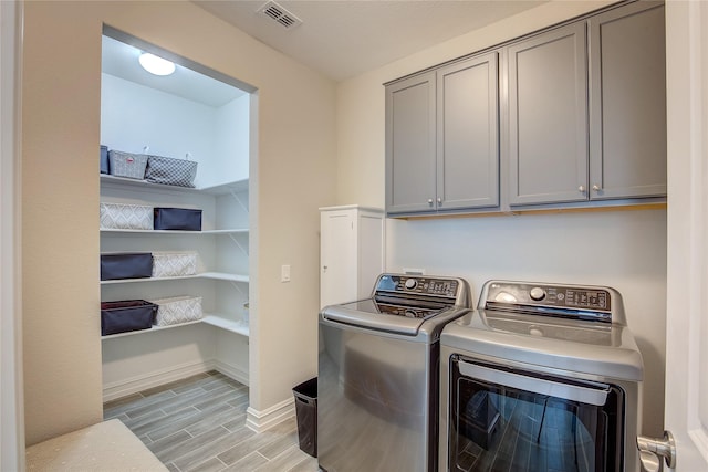 laundry room with visible vents, baseboards, wood tiled floor, cabinet space, and washer and clothes dryer