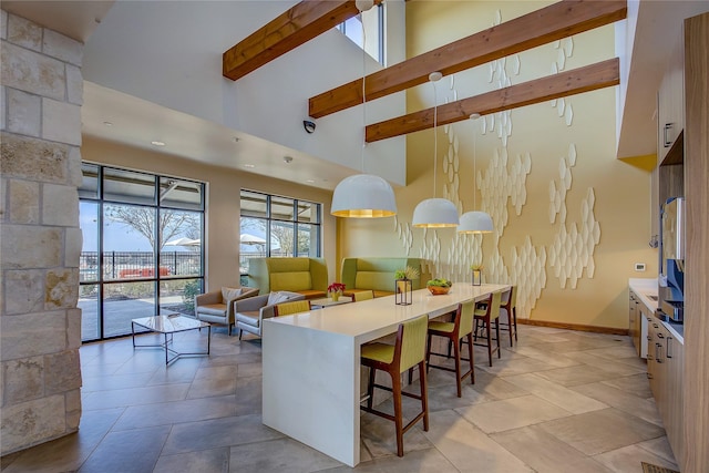 kitchen with a kitchen bar, a high ceiling, hanging light fixtures, and beamed ceiling